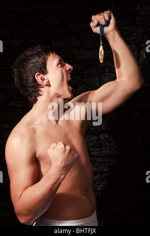 Männlicher Athlet Goldmedaille hochhalten und Stanzen Luft in Aufregung auf einen Sieg Stockfoto