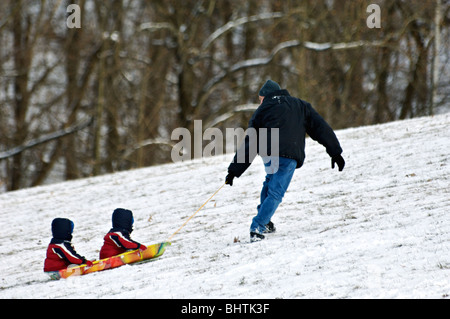 Vater ziehen zwei Kleinkinder bergauf auf Schlitten in Cherokee Park in Louisville Stockfoto