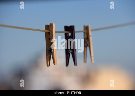 drei Wäscheklammern an einer Wäscheleine vor einem strahlend blauen Himmel über der Stadt hängen Stockfoto