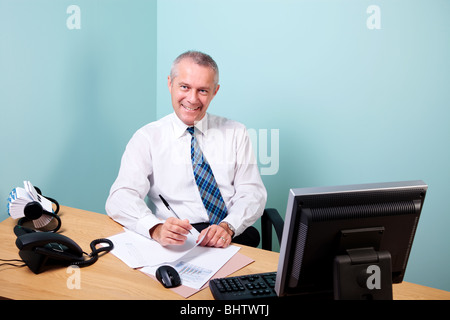 Reife Geschäftsmann saß an seinem Schreibtisch mit Blick auf die Kamera und lächelnd Stockfoto