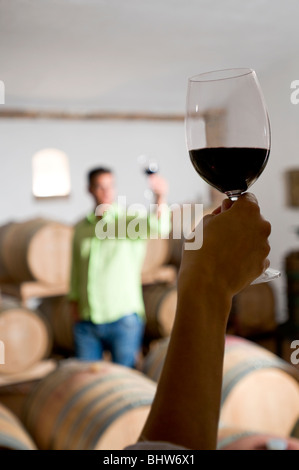 Junge Frau Hand mit Glas Rotwein mit jungen Mann im Hintergrund hält sein Weinglas Stockfoto