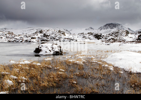 Blick auf große Giebel über InnominateTarn auf Heu im Winter mit Schnee und Eis auf die umliegenden Berge Stockfoto