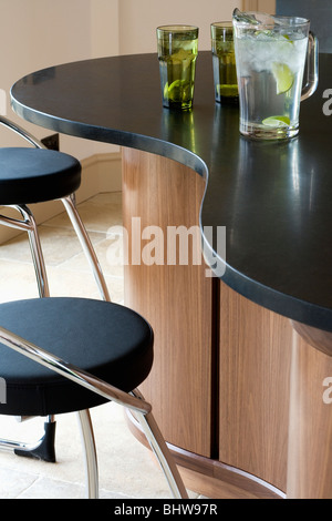 Nahaufnahme von Chrom und schwarzem Leder Hocker am geschwungenen Theke mit Krug mit Fruchtsaft auf schwarzem Granit-Arbeitsplatte Stockfoto