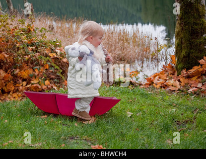 Diese niedlichen Kleinkind Mädchen ist im Herbst in der Nähe von einem See mit einem Burgunder Schirm draußen spielen und halten Sie ihr Tier Stofftier. Stockfoto