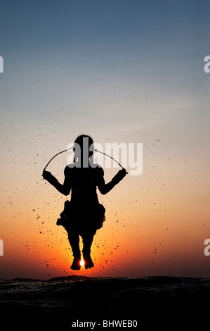 Silhouette eines indischen Mädchens überspringen in Wasser bei Sonnenuntergang. Indien Stockfoto