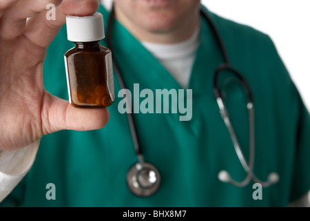 Mann trägt medizinische Peelings und Stethoskop holding und mit Blick auf eine kleine Flasche Pillen Stockfoto