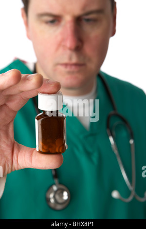 Mann trägt medizinische Peelings und Stethoskop holding und mit Blick auf eine kleine Flasche Pillen Stockfoto