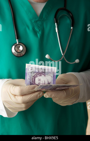 Mann mit medizinischen Peelings und Stethoskop zählt 20 Pfund Sterling Banknoten Junior Doktor Lohngeld Geld Stockfoto