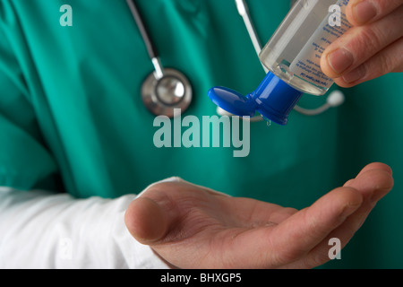 Der Mann, der medizinische Schrubben und Stethoskop trägt, schüttet Alkohol Gel Handdesinfektionsmittel aus einer tragbaren Flasche in seine Hände Stockfoto