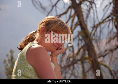 Diese Mitte Alter blonde Frau im Freien ist tief in Gedanken versunken in diesem ruhigen Foto mit einem Hintergrund Baum von konzentrieren absichtlich f Stockfoto