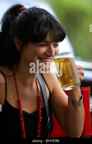 Mitte der zwanziger Jahre hispanic Frau lachen, trinken ein volles Glas Bier in einem Straßencafé Stockfoto