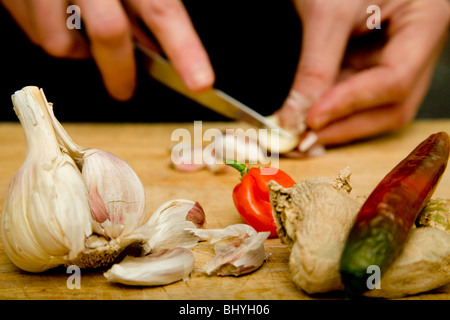 Ein Mann Kochen Gewürze vorbereiten, scotch Knoblauch Chilis Bonnet Ingwer auf ein Schneidbrett aus Holz Stockfoto