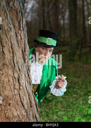 Kobold mit einer Pfeife versteckt sich hinter einem Baum in einem Wald Stockfoto