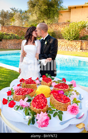 Braut und Bräutigam küssen am Tag der Hochzeit in der Nähe von Pool und Hochzeitstorten Stockfoto