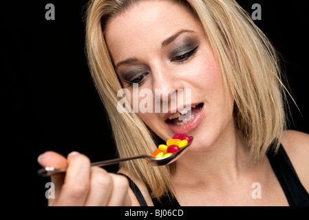 blonde Frau, die einen Löffel von Pillen oder Süßigkeiten Stockfoto