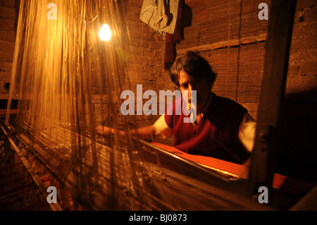 Mann auf einer Hand weben Webstuhl machen Saris an der Nachtzeit durch gelbe Kunstlicht Stockfoto