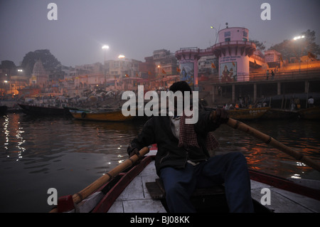 Ein junger Mann Zeilen vorbei an Heiligen Ghats von Varanasi am Fluss Ganges kurz vor Sonnenaufgang Stockfoto