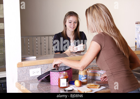 Tochter zu frühstücken, während Mama Mittagessen für die Schule macht Stockfoto