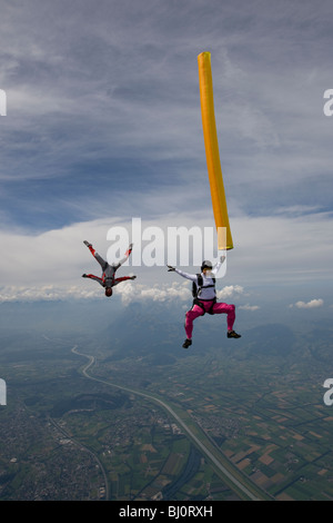 Fallschirmspringer mit orange Luftschlauch fliegt hoch in den Himmel, die anderen Taucher um das Rohr im Kopf unten Position erfasst ist. Stockfoto