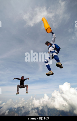 Fallschirmspringer Kopf fliegen liegen ein Team und orange Luftschlauch über eine spektakuläre Berg- und Cloud-Landschaft zu halten. Stockfoto