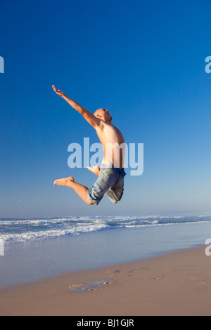 Junger Mann springt am Strand Stockfoto