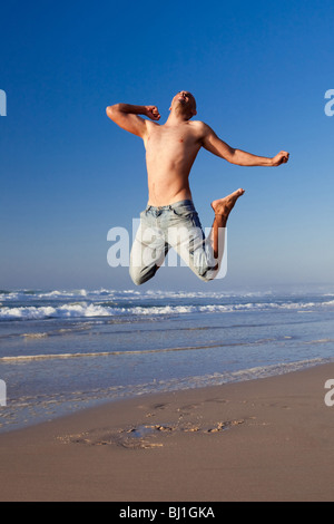 Junger Mann springt am Strand Stockfoto