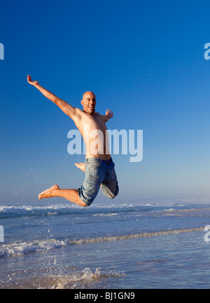 Junger Mann springt am Strand Stockfoto