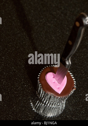 ein Valentinstag Schokolade Cupcake mit ein Herz mit einem Messer erstochen Stockfoto