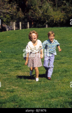 weißen Bruder und Schwester im Alter von 10 und 9 halten die Hände wie sie laufen über den Rasen des Park Lachen fröhlicher Junge Mädchen Stockfoto