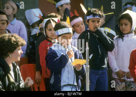 Acht Jahre Alter spanischer junge Mann liest und spricht in Mikrofon Schulversammlung.  Er trägt indianischen Stil Kopfschmuck Stockfoto