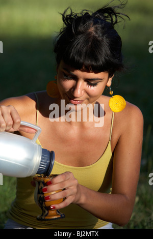 junge spanische Latin Frau gießt heißes Wasser aus einer Thermoskanne in einem Mate-Kürbis im Park in Buenos Aires Argentinien Stockfoto