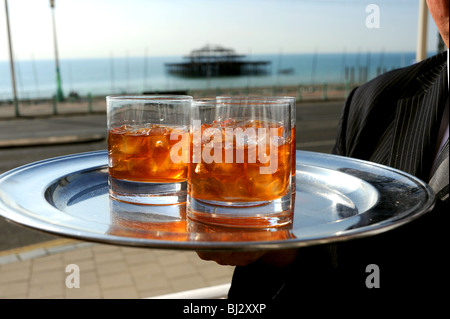 Tumbler Gläser Whisky mit Klumpen von Eiswürfeln auf einem Tablett vor West Pier Brighton Seafront von hand gehalten Stockfoto