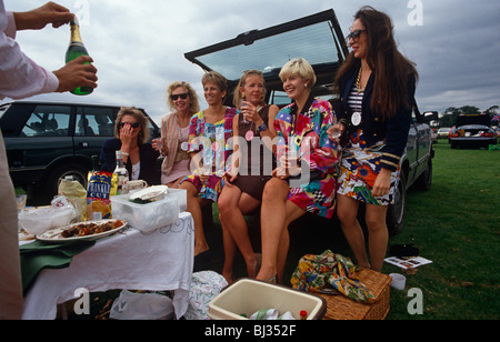 Sechs Damen warten auf die Öffnung einer Flasche Champagner von einem unsichtbaren männlichen Freund im Laufe des Tages an Royal Ascot Pferderennen Woche. Stockfoto