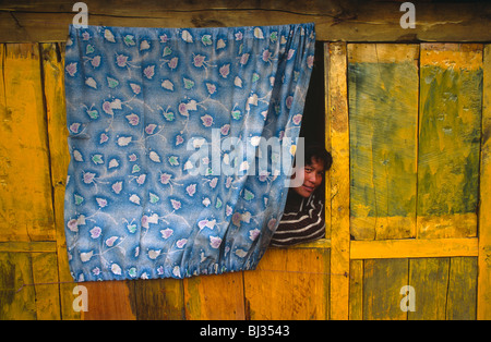 Ein junger Mann Nepali späht heraus aus einem Vorhang, mit einer unsichtbaren Nachbarn in einem abgelegenen Dorf in der Nähe von Ulleri zu sprechen. Stockfoto