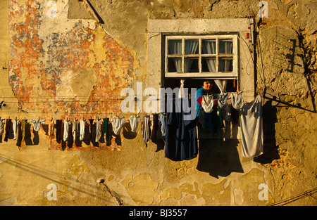 Hoch über den Straßen lehnt der alten Lissabon, eine Portugiesin aus ihrem Fenster zu hängen ihre Wäsche im Viertel Bairro Alto, Stockfoto