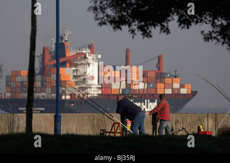 Ein Hapag-Lloyd-Container-Frachtschiff navigiert vorbei an zwei Fischer am südlichen Ufer der Themse bei Gravesend. Stockfoto