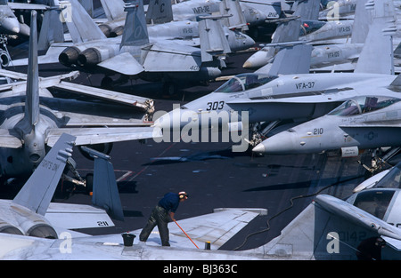 Ein einsamer Seemann Abbürsten der schmutzigen Oberflächen der geparkten F/A-18 C Hornets und s-3 Wikinger auf dem Flugzeugträger der US Navy. Stockfoto