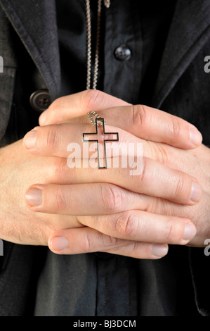 Betende Hände halten eine Halskette mit einem Kreuz-Anhänger Stockfoto