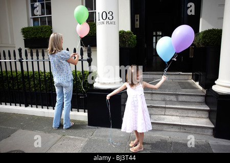 Ein junges Mädchen und ihre Mutter bereiten für den Kindergeburtstag von Ballons zum Geländer am Eaton Place, Belgravia zu binden. Stockfoto