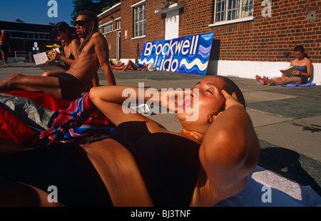 Durch den Mund atmen, hebt eine Dame in einem Bikini Kostüm den Kopf, die für mehr Sit-ups im Brockwell Lido unterstützt. Stockfoto