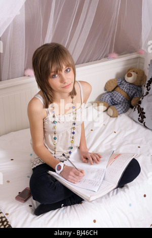 14 Jahre alten Teenager-Mädchen sitzen gekreuzt Beinen auf ihrem Bett, die Hausaufgaben. Stockfoto