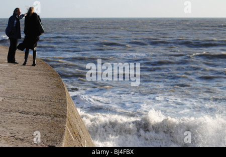 Ein paar blicken auf stürmischer See von den Cobb Hafen Wänden, Lyme Regis, Dorset, England Stockfoto