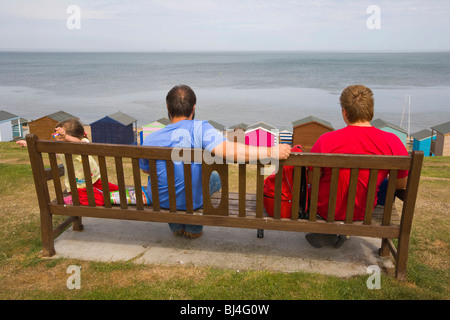 Familie auf einer Bank mit Blick auf Strand, Hütten und Meer bei Tankerton in der Nähe von Whitstable, Kent, England, Vereinigtes Königreich, Europa Stockfoto