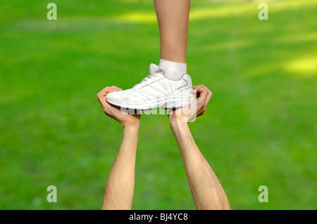 Zwei starke männliche Hände halten einen weiblichen Fuß. Teamarbeit, Unterstützung, Hilfe, Gymnastik, Wettbewerb-Konzepte. Stockfoto