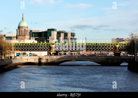 Der DART-Zug fährt über eine Brücke über den Fluss Liffey mit der Irish Financial Services Zentrum & Customs House im Hintergrund Stockfoto