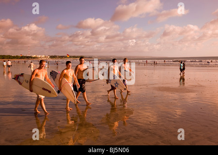 Indonesien, Bali, Kuta, Strand, Gruppe von männlichen Surfer bei Sonnenuntergang entlang nassen Sand am Ende der Tage Surfen Stockfoto