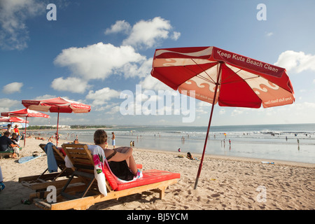 Indonesien, Bali, Kuta, Strand, Frau sitzt auf der Liege im Schatten der halten Kuta Strand sauber Sonnenschirm Stockfoto