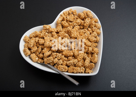 Herzförmige Müslischale oder Schale mit Löffel und Getreide auf schwarzem Hintergrund. Stockfoto