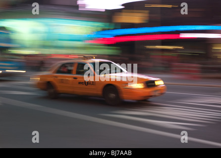 Ein gelbes Taxi ist eine Unschärfe, da es durch die Lichter des Times Square bei Nacht in New York City stürmt. Stockfoto