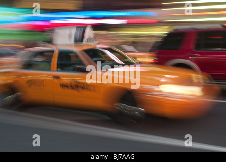 Ein gelbes Taxi ist eine Unschärfe, da es durch die Lichter des Times Square bei Nacht in New York City stürmt. Stockfoto